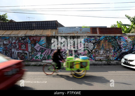 Jogjakarta, Indonesien - 22. Juni 2018: eine Rikscha Fahrer Fahrten Vergangenheit Graffiti und Verkehr auf Tirtodipuran Straße in Jogyakarta Stockfoto