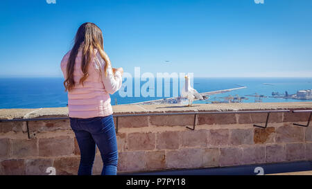Junge Mädchen Fütterung eine Möwe auf Montjuic Berg. Gull hoch Öffnung seiner Peak von Mädchen Hand zu essen, blau klares Wasser und wunderbaren Horizont lin Stockfoto