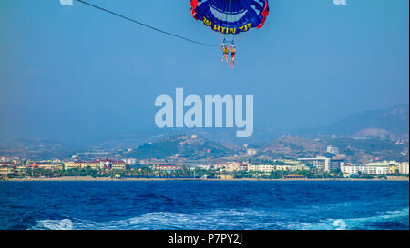 ALANYA, Türkei - August 03, 2016 - Vater und Sohn parasailing am tropischen Strand im Sommer. Paar unter Fallschirm hängenden Mitte der Luft. Spaß haben. Tropische Stockfoto