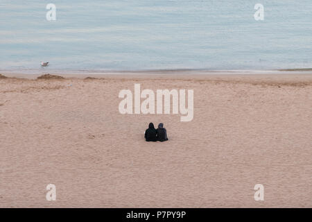 Zwei Frauen mit hijabs Sitzen auf den Rücken in den sand Quemado Strand bei Sonnenuntergang, Al Hoceima, Marokko Stockfoto