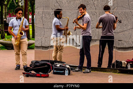 Street Performer in Amsterdam, mit Reflexion an der Wand und spielte Geige und Saxophon Musik Stockfoto