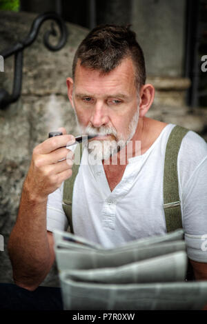 Portrait von gut aussehenden bärtigen Mann in seinem 50s Rauchen eine Leitung und eine Zeitung lesen Stockfoto
