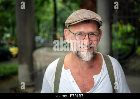 Portrait von Stattlichen lächelnd bärtiger Mann mit Hut und Brille in seinem 50s Stockfoto