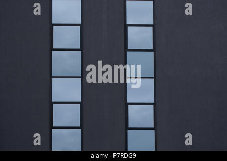 Dunkle graue Betonwand mit zwei vertikalen Fenstern Zeilen als Hintergrund. Architektonisches detail. Stockfoto