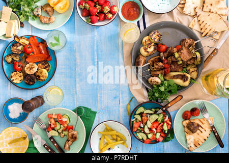 Rahmen der Shish Kebab, gegrilltes Gemüse, Salate, Snacks, Erdbeeren und hausgemachte Limonade auf Blau Holz- Tabelle, Ansicht von oben Stockfoto