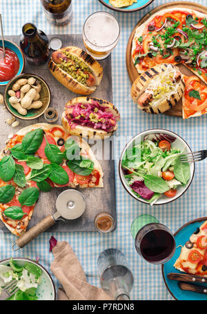 Verschiedene hausgemachte Pizza, Hot Dogs, Rotwein, Bier und Snacks für Bier auf den Tisch, Ansicht von oben. Tisch Konzept Stockfoto