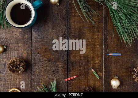 Rahmen der Tasse Kaffee, Tannenzapfen, Buntstifte, Weihnachtskugeln und Weihnachtsbaum Niederlassungen auf braunem Holz- Hintergrund, Ansicht von oben. Weihnachten hinterg Stockfoto