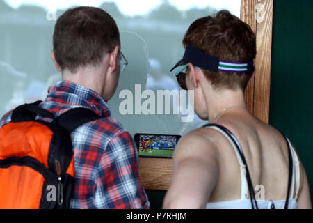 Tennisfans sehen sich am sechsten Tag der Wimbledon-Meisterschaft im All England Lawn Tennis and Croquet Club, Wimbledon, das Viertelfinale der Fußball-Weltmeisterschaft gegen Schweden am Telefon an. Stockfoto