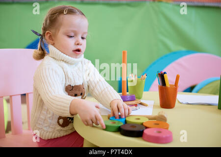 Kleines Mädchen Zeichnung mit Buntstifte - Sitzen am Tisch mit ihr Spielzeug tragen Stockfoto