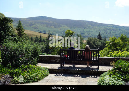 Ein Paar sitzt auf einer Holzbank an der Simon von Seat im Parcevall Hall Gardens, Skyreholme, Appletreewick, Wharfedale, Yorkshire, England, UK. Stockfoto