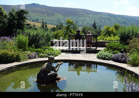 Ein Paar sitzt auf einer Holzbank an der Simon von Seat im Parcevall Hall Gardens, Skyreholme, Appletreewick, Wharfedale, Yorkshire, England, UK. Stockfoto