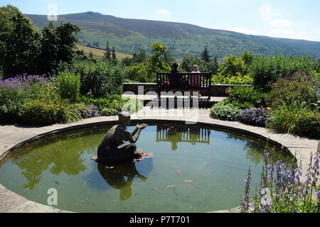 Ein Paar sitzt auf einer Holzbank an der Simon von Seat im Parcevall Hall Gardens, Skyreholme, Appletreewick, Wharfedale, Yorkshire, England, UK. Stockfoto