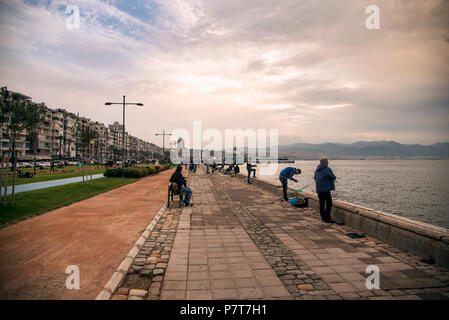 Izmir, Türkei - Oktober 28, 2017: Blick über Izmir Alsancak Fähre und Leute angeln und sitzen in der Nähe von Waters Edge mit bewölktem Wetter. Stockfoto