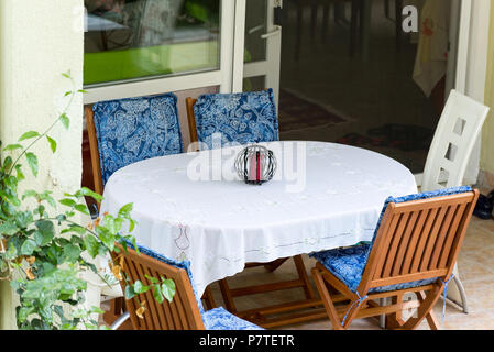 Tisch mit weißer Tischdecke und Stühle in der Nähe von Haus bedeckt Stockfoto
