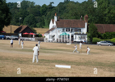 Tilford, Surrey, Großbritannien. Juli 2018. Während die Hitzewelle anhält, hatten die Leute Spaß in der Sonne an einem schönen Sonntagnachmittag im hübschen Dorf Tilford. Viele kühlten sich im Fluss ab oder sonnen sich, während ein Cricket-Spiel auf dem Dorfgrün gespielt wurde. Stockfoto