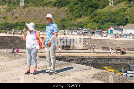 Lyme Regis, Dorset, Großbritannien. 8. Juli 2018. UK Wetter: Weitere glühend heiß und sonnig Sonntag in Lyme Regis. Die Jurassic Coast braten wieder als Besucher und Einheimische in Scharen zu den Strand auf Weiteres sizzling Sonntag an der Südküste. Ein paar machen Sie einen Spaziergang entlang der berühmten Cobb in der heißen Sonne. Credit: Celia McMahon/Alamy leben Nachrichten Stockfoto