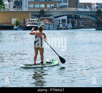 Themse, Hampton Wick, London, England, Vereinigtes Königreich, 8. Juli 2018. UK Wetter: Leute genießen, sich auf der Themse an einem Sonntag Morgen in der heißen Sonne Hitzewelle. Eine ältere Frau Paddle Boarding in Richtung Kingston Bridge Stockfoto