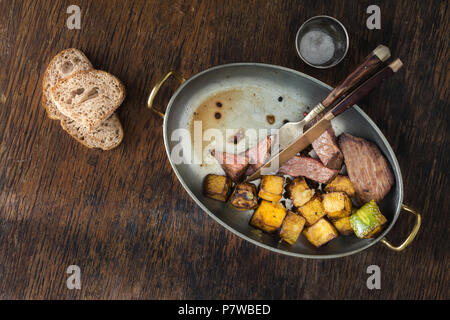 Ansicht von oben Rindersteak mit gebratenen Kürbis in der Pfanne auf dunklem Hintergrund Stockfoto