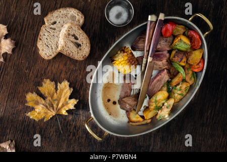 Beef Steak mit Bratkartoffeln und Gemüse in der Pfanne auf dunklem Hintergrund, Ansicht von oben. Tisch Konzept Stockfoto