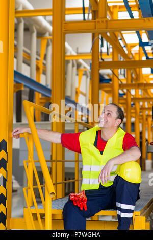 Arbeitnehmer in Gelb reflektierende Anzug mit gelben Helm in einer Fabrik sitzen und Suchen Stockfoto