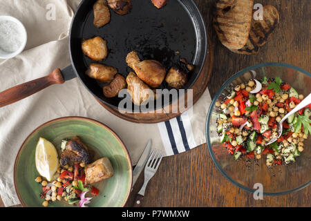 Gebratenes Fleisch in der Pfanne auf Holztisch mit frischem Gemüse Salat von schwarzen Quinoa und Kichererbsen, Ansicht von oben. Einfache und gesunde Hausmannskost Stockfoto