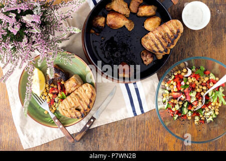 Stück Braten in der Pfanne auf Holztisch mit frischem Gemüse Salat von schwarzen Quinoa und Kichererbsen, Ansicht von oben. Gesunde Hausmannskost Stockfoto