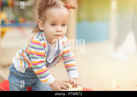 Ein kleines Mädchen mit zwei Schwänze in einem gestreifte Bluse spielt eine Sommer sonnigen Tag auf dem Spielplatz Sommer Familie Freizeit Stockfoto