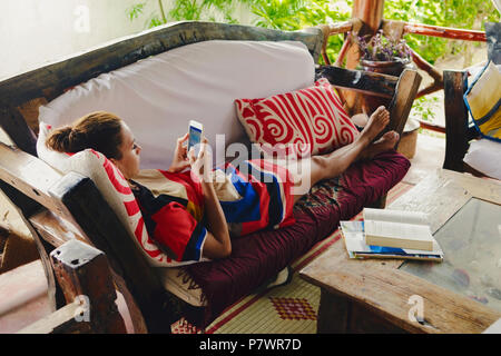 Junge Frau auf dem Sofa in der Vorhalle kommuniziert in sozialen Netzwerken Stockfoto