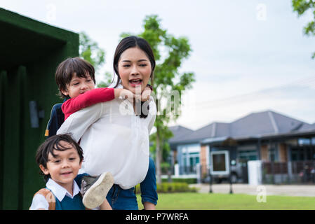 Einzelne Mamma tragen und Spielen mit Ihren Kindern im Garten mit grünen Wand Hintergrund. Die Menschen und Lebensstile Konzept. Glückliche Familie und Home sweet Ho Stockfoto