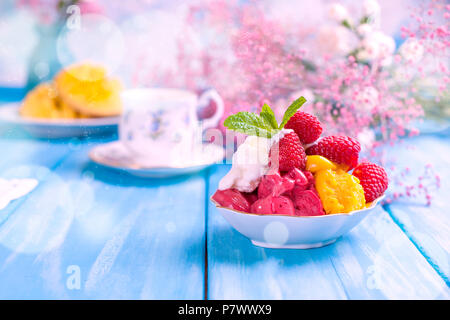 Obst Eis mit Himbeeren und Mango. Blumen und reife Mango auf einem blauen Hintergrund aus Holz. Frühstück ist süß und Kaffee. Stockfoto