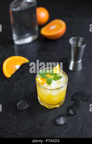 Gin und Orangensaft Cocktail auf schwarzen Hintergrund. Erfrischende Sommer Cocktail mit Wodka, Eis, Orange und Minze. Stockfoto