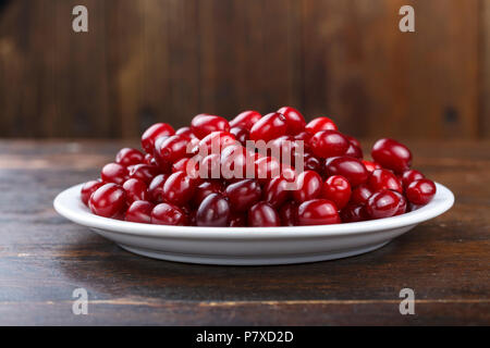 Carneol cherry Hartriegel genießbare Früchte. Frische Hartriegel (Cornus sanguinea) Beeren in runde weiße Schüssel auf dunklem Hintergrund. Stockfoto