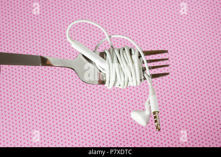 Weiße Kopfhörer und Gabel auf einem rosa Hintergrund mit Polka dotsd, close-up Stockfoto