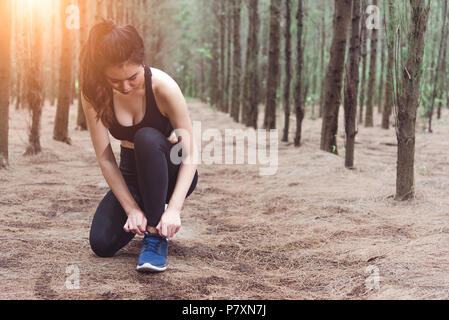 Frau Schnürsenkel binden beim Joggen im Wald zurück mit Trinkwasser Flasche neben Ihrem. Sneakers Seil binden. Die Menschen und Lebensstile Konzept. Gesundheit Stockfoto