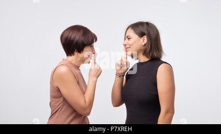 Frauen Mutter und Tochter klatschen und sagen ein Geheimnis über grauer Hintergrund isoliert. Stockfoto