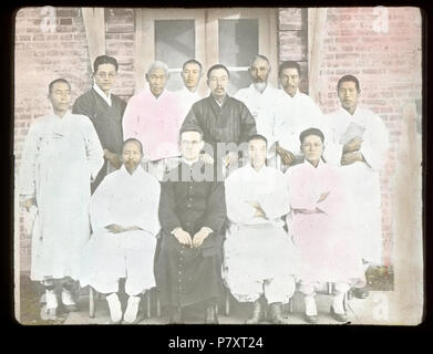 Englisch: Group Portrait von Fr. John E. Morris, MM, und elf Koreanische Männer, Korea, Ca. 1920/1940 eingefärbte Laterne Folie von P. John E. Morris, MM, mit elf koreanischen Männern. Fr. Morris trägt eine Soutane und Gläser. Er ist einer von vier Männern in der ersten Reihe sitzt. Die zwei Männer, die zu seiner Linken haben die Arme über der Brust gekreuzt. In der hinteren Zylinderreihe auf der rechten Seite ist ein Mann hält ein Buch. Die Gruppe stellt sich vor die Tür zu einem Backsteingebäude. Fotograf: unbekannt Thema (Stichwort): indigene Völker und Klerus; Gruppe Porträts Dateiname: MFB-LS0488 Abdeckung Datum: ca. 1920/1940 Thema Stockfoto