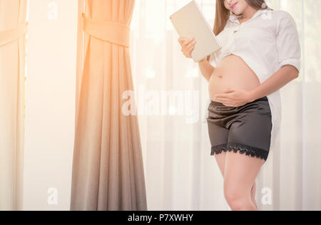 Schwangere Frau stehen und das Tablett mit ihrem touch Balg in Ihr Haus, Familie und Gesundheit Konzept Stockfoto