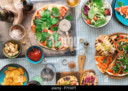 Tisch mit verschiedenen köstlichen Speisen. Italienische Pizza, Hot dog Gegrilltes, Salat, Wein, Bier und Snacks für Bier, Ansicht von oben Stockfoto