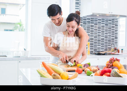 Asiatische Liebhaber oder paar Kochen und Schneiden von Gemüse in der Küche Zimmer. Mann und Frau einander im Hause. Urlaub und Hochzeitsreise Konzept. Valenti Stockfoto