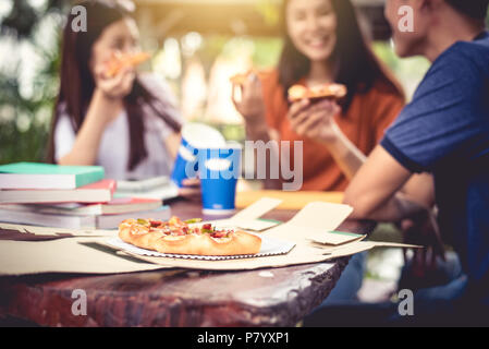 Drei asiatische Menschen genießen essen Pizza an im Freien nach nachhilfe Klasse. Bildung und Party Konzept. Essen und Getränke Thema. Glück lifestyle Thema. Stockfoto
