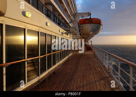 Abend auf Deck 7 der "Queen Mary 2", wie die Einstellung, die Sonne kommt hinter den Wolken das Deck und das Meer zu beleuchten; Leben Boote Hand über Deck. Stockfoto