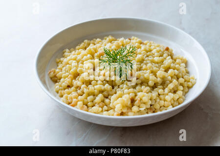 Gekochten Couscous mit Dill, serviert in weiße Platte/Türkischen Kuskus. Traditionelle biologische Lebensmittel. Stockfoto