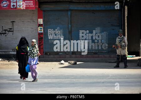 Kaschmir einheimischen vorbei ein indischer Polizist Wache während auferlegten Beschränkungen der zweite Tod Jahrestag der Rebel commander Burhan Nassim Wani in Srinagar. Burhan und seine Mitarbeiter waren an diesem Tag im Jahr 2016 Auslösen einer massiven anti-Indien Aufstand in Kaschmir getötet. Während des Aufstandes mehr als 90 Menschen wurden getötet, rund 15.000 wurden verletzt, unter ihnen 950 Augenverletzungen mit pellet Gewehre empfangen. Stockfoto