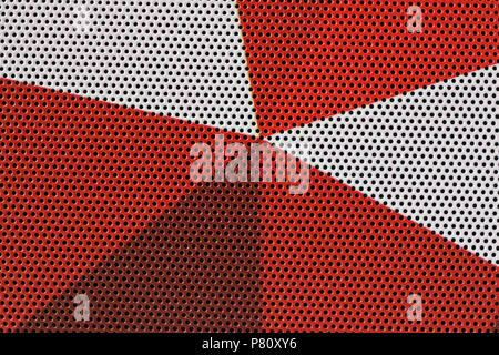Tausende von kleinen Öffnungen werden in einer metallischen Oberfläche, die in rot und weiß bemalt ist. Studio Makroaufnahme Stockfoto