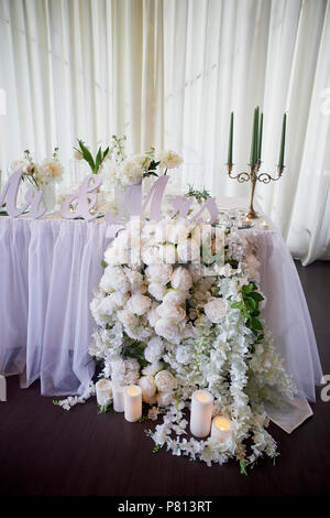 Blumengirlande von Pine-förmige Rosen hängt von der Tabelle. Hochzeit Dekoration, Floristik. Kandelaber mit grünen Kerzen. Die Inschrift Mr. und Mrs. Die Tischdekoration mit Chiffon Stockfoto