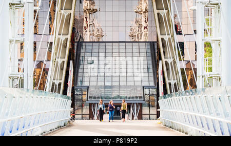 Drei Frauen sprechen und gemeinsam zu Fuß entfernt von Bürogebäude über eine Brücke an der Salford Quays, Manchester möglicherweise unter eine Mittagspause. Stockfoto