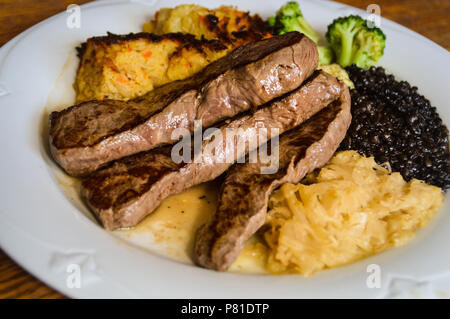 Einfache deutsche Gericht zum Mittagessen aus Schweinefleisch steak Slices, Sauerkraut, schorles und Beluga Salat mit Linsen Stockfoto