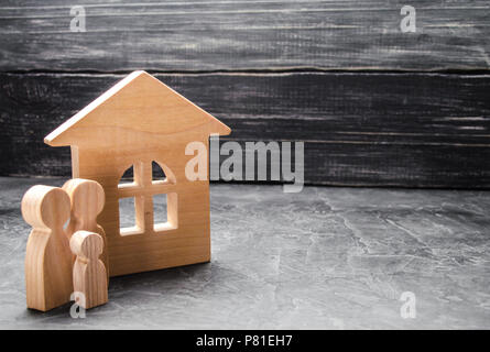 Eine junge Familie mit einem Kind steht in der Nähe des Hauses. Holzhaus und Zahlen von Menschen. Das Konzept der Gehäuse suchen, Mieten, Kaufen. Bewegen. Loa Stockfoto