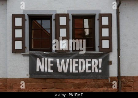 Kandel, Deutschland. 07 Juli, 2018. Ein Banner reading "Nie wieder" hängt an einem Haus in Kandel. Rund 200 Menschen von Rechten Organisationen protestierten für das 10. mal in der Stadt Kandel in der Pfalz gegen Flüchtlinge, Ausländer und der deutschen Regierung. Sie forderten mehr Sicherheit von Deutschen und Frauen aus der angeblichen Zunahme der Gewalt durch Flüchtlinge. An die Stelle der Protest wurde gewählt, weil der 2017 Kandel erstechen Angriff, bei dem ein 15 Jahre altes Mädchen von einem Asylbewerber getötet wurde. Sie wurden von rund 200 anti-faschistischen counter-Demonstranten aus verschiedenen politischen Parteien belästigt und Stockfoto