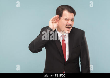 Unternehmer hören einen anderen Mann. Was Sie sagen, ich kann Sie nicht hören, ist es hier sehr laut. Studio erschossen. auf blauem Hintergrund isoliert. Geschäftsmann mit b Stockfoto